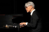 Ryuichi Sakamoto plays the piano in Tokyo's Tennozu district on March 29. (Shiro Nishihata)